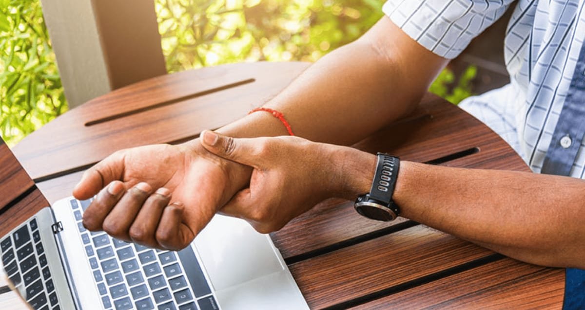 WALANT Carpal Tunnel Release in Delray Beach: A Patient’s Guide to the Wide-Awake Approach Person at a laptop gripping a painful wrist, a common sign of carpal tunnel syndrome treated with in-office WALANT release at Tyrance Orthopedics in Delray Beach.