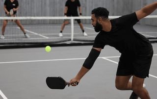 Pickleball player lunging to return the ball with a paddle during a match while wearing an elbow sleeve, illustrating common pickleball injuries seen at Tyrance Orthopedics in Palm Beach.