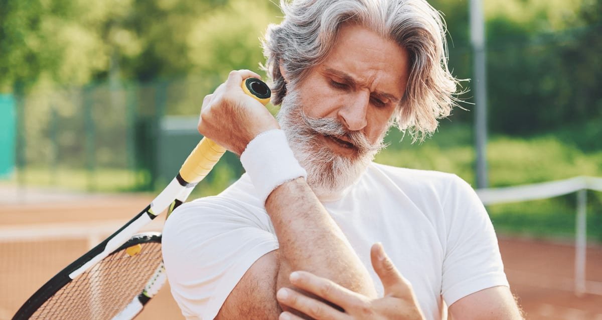 PRP for Tennis Elbow: A Regenerative Alternative When Cortisone and Rest Are Not Working Older tennis player on a clay court holding his racket and gripping his painful elbow, a sign of tennis elbow treated with PRP at Tyrance Orthopedics in Delray Beach.