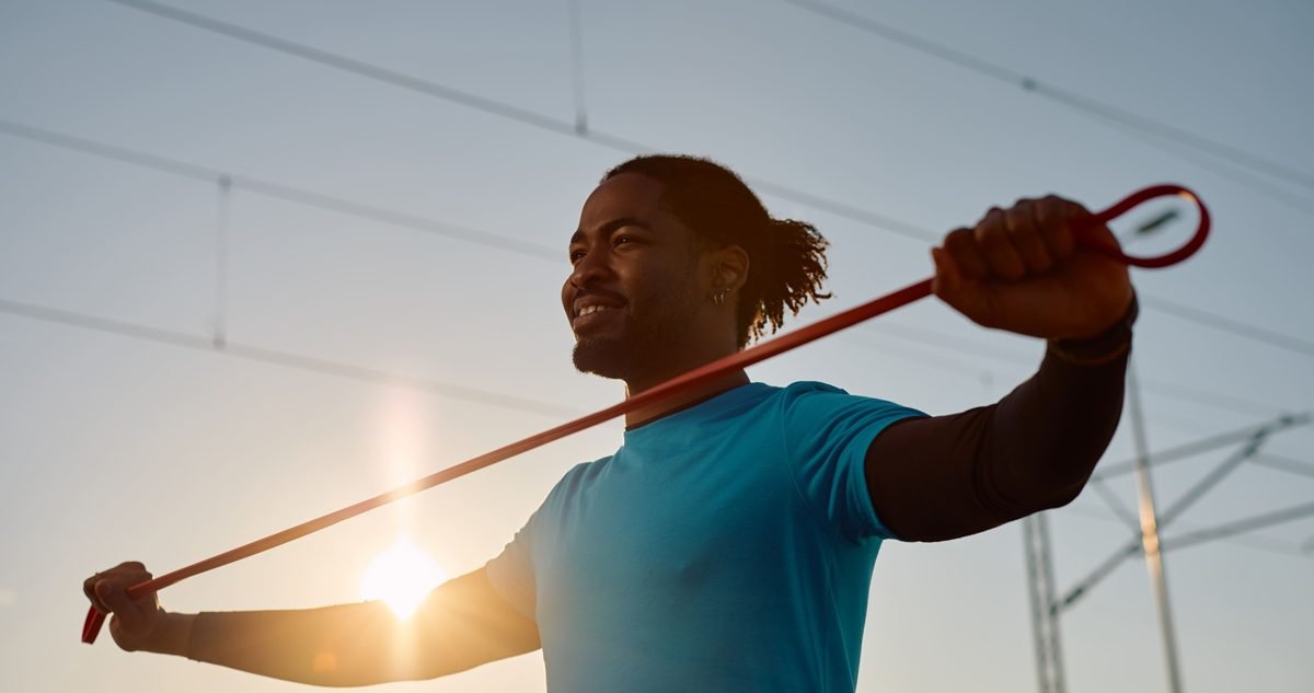 AC Joint Arthritis Treatment Options Athlete drawing a resistance band across the shoulders outdoors, the kind of controlled loading that keeps an arthritic AC joint working.