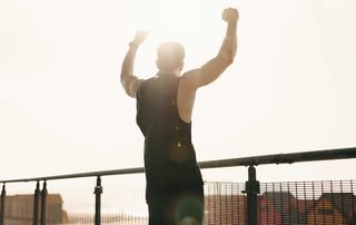 Man raising both arms on a waterfront path at sunrise, the overhead reach a repaired rotator cuff is meant to give back.