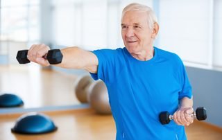 Older man raising a dumbbell to shoulder height in a gym, the kind of strengthening that keeps an arthritic shoulder moving.