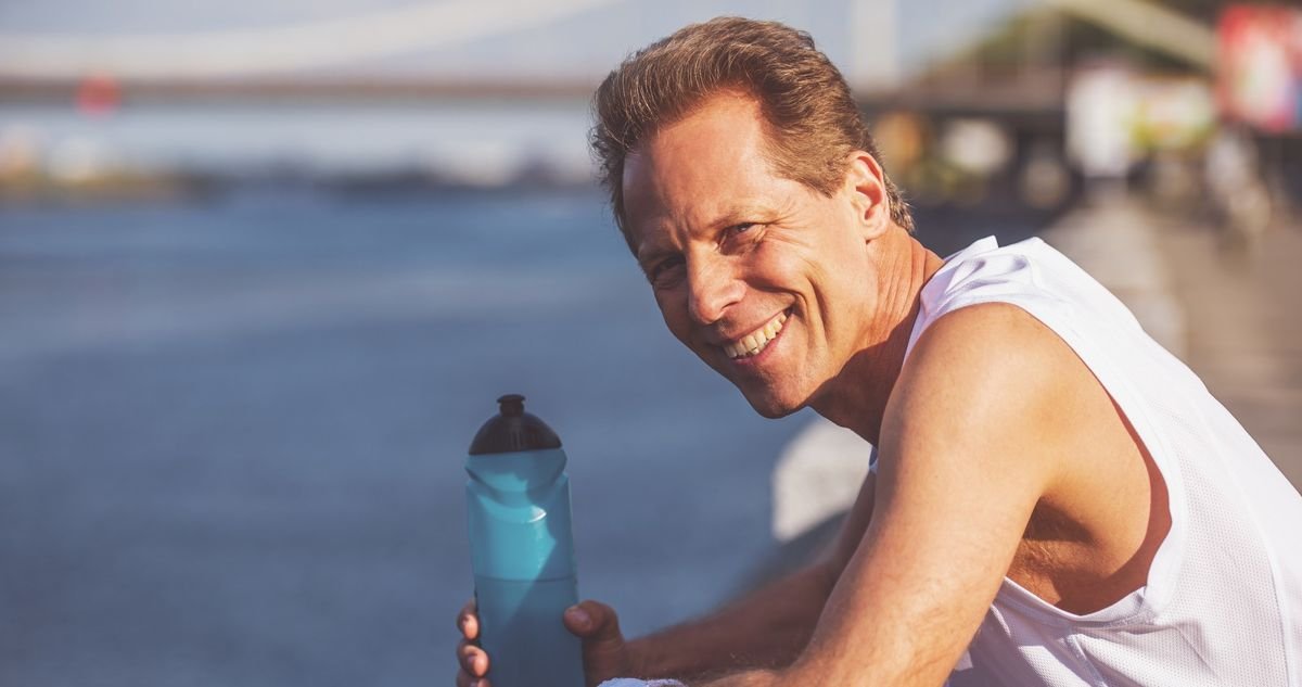 Planned recovery between training sessions after 40 Smiling runner over 40 resting on a waterfront railing with a water bottle between training efforts